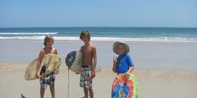 three boys holding surfboards on the beach